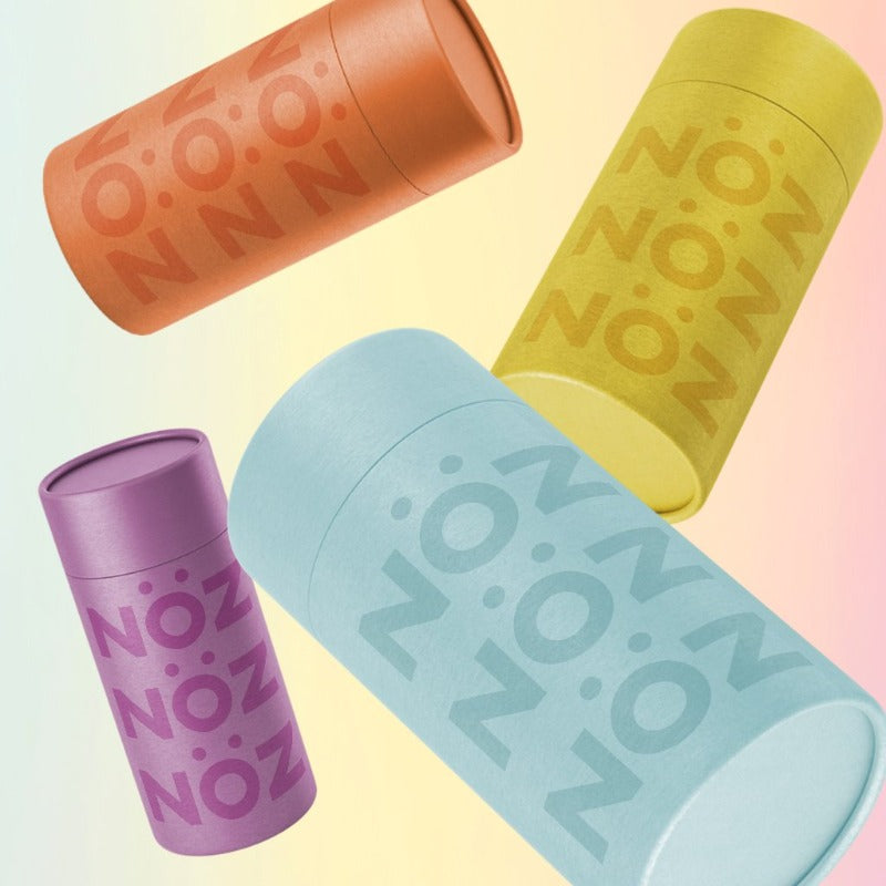 Four Nöz sunscreen bottles, in orange, purple, blue, and yellow, angled in the air with a freezeshot